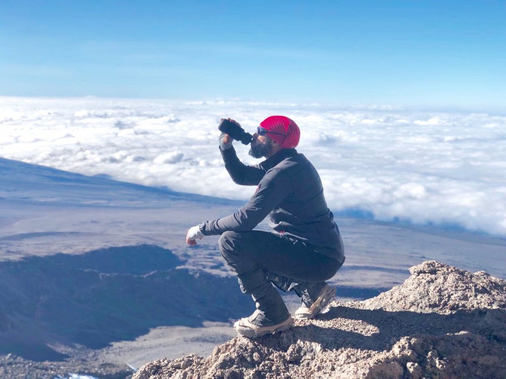 Samir Souadji au sommet d'une montagne regarde les nuages en buvant dans sa gourde