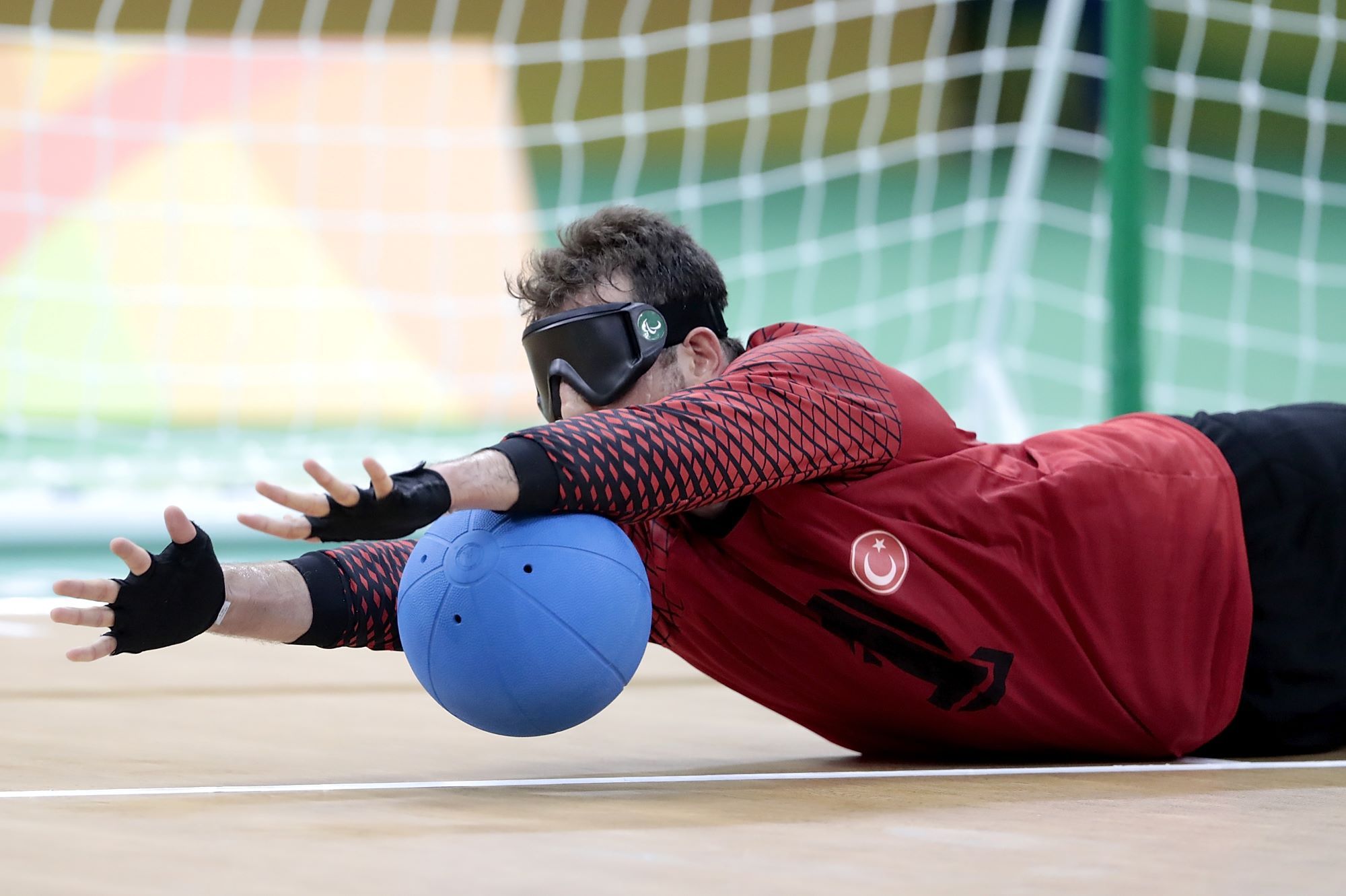 Un joueur de goalball arrête le ballon en se couchant au sol, les bras tendus