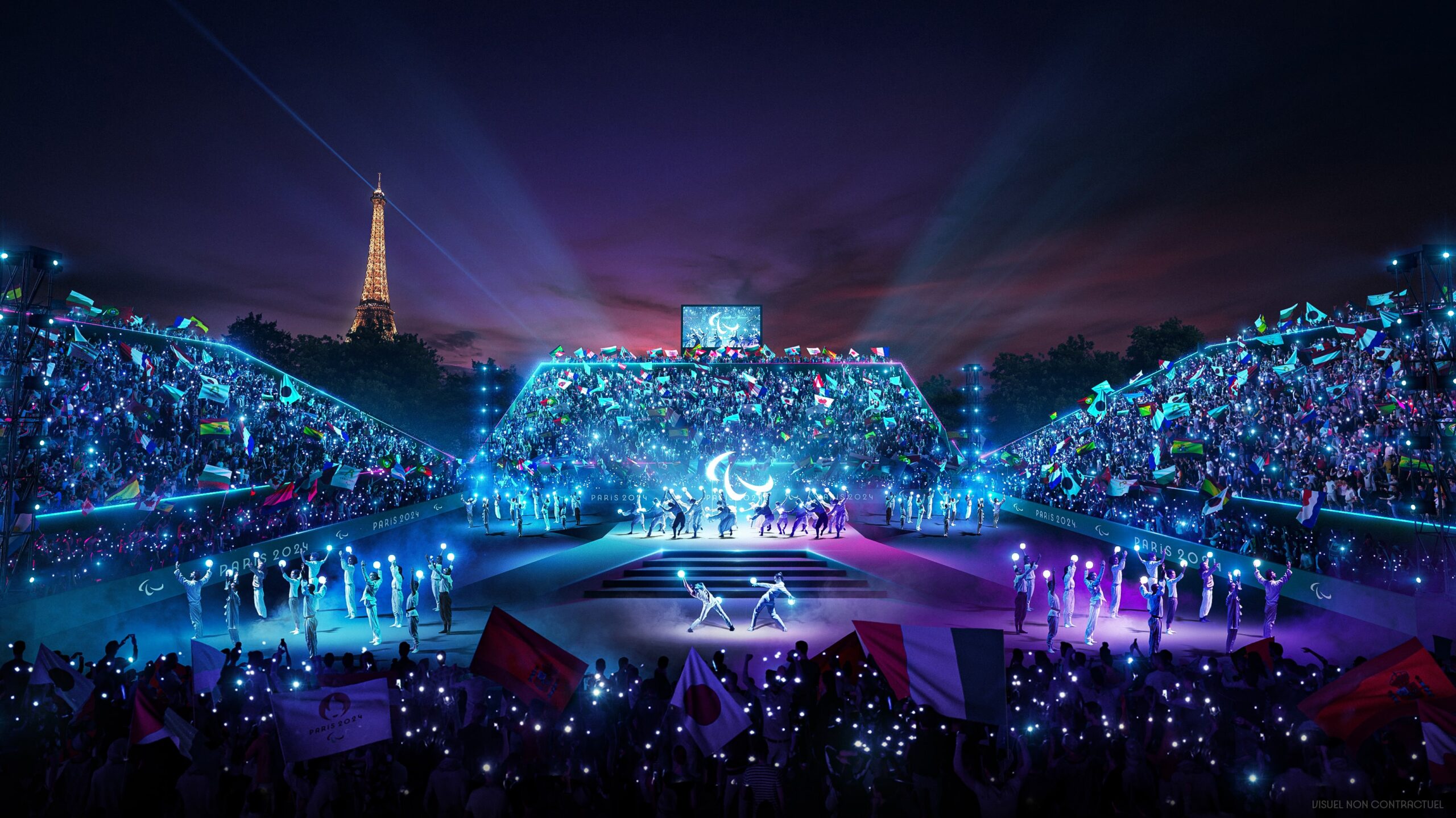 View of the Place de la Concorde at night. A stage with dancers holding lights. The public in the stands are holding flags. The Eiffel Tower can be seen in the background.